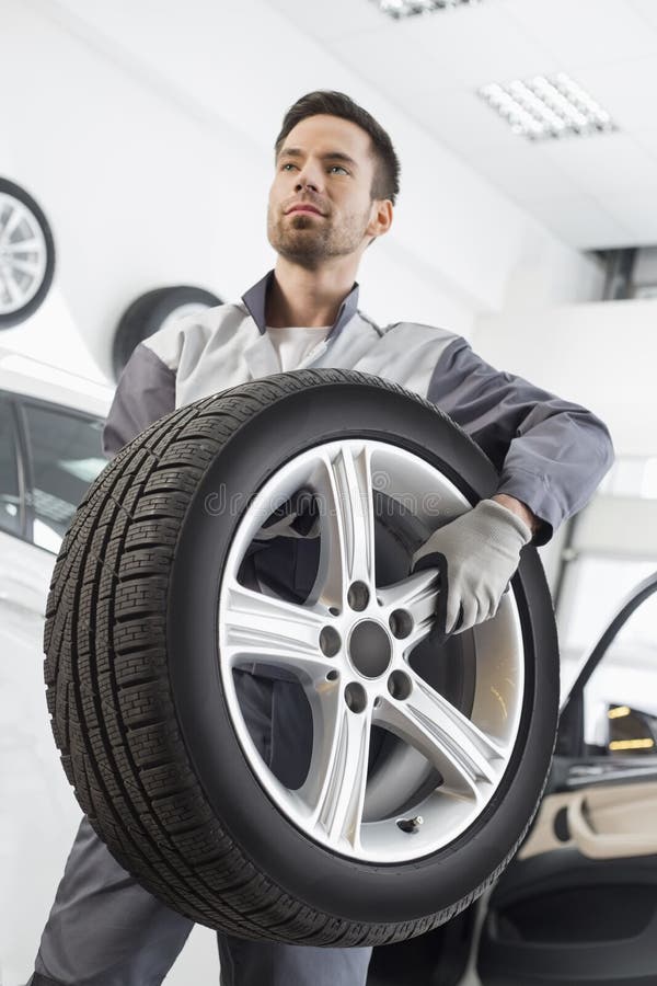 Young Maintenance Engineer Carrying Tire in Automobile Store Stock