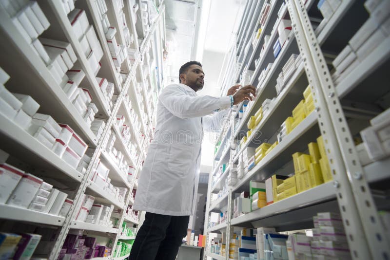 Young Male Chemist Arranging Products In Shelves At Pharmacy