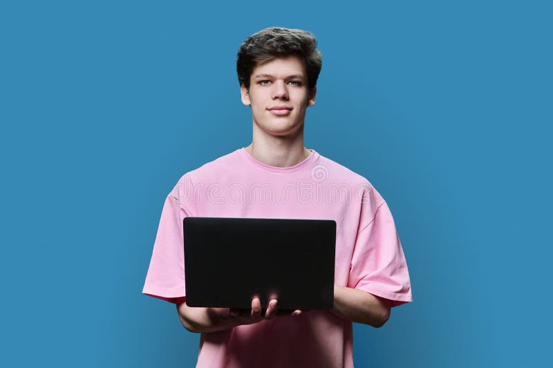 Young male college student using laptop, blue background stock photo