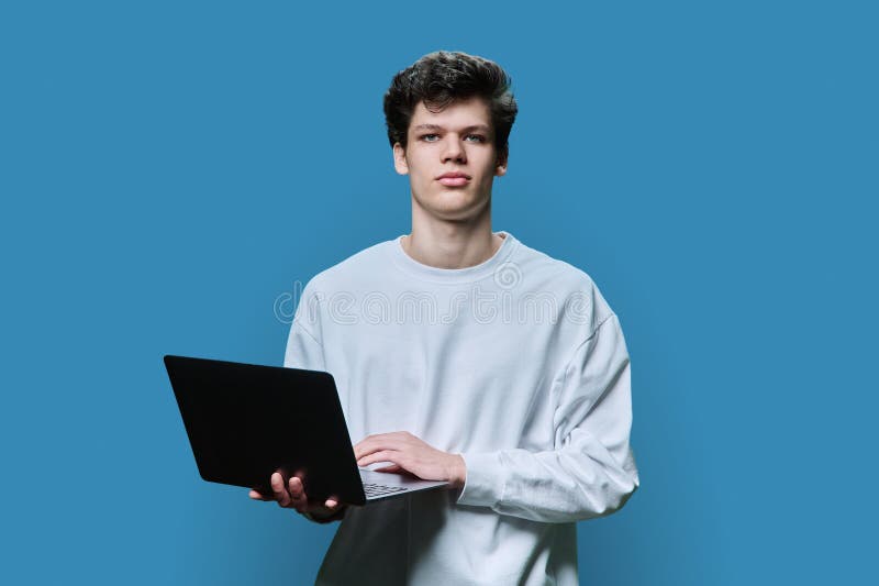 Young male college student using laptop, blue background stock photography