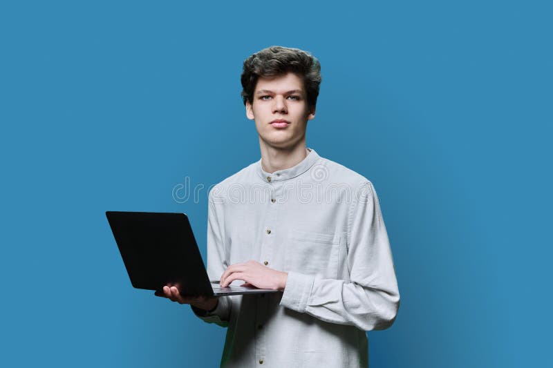Young male college student using laptop, blue background stock image