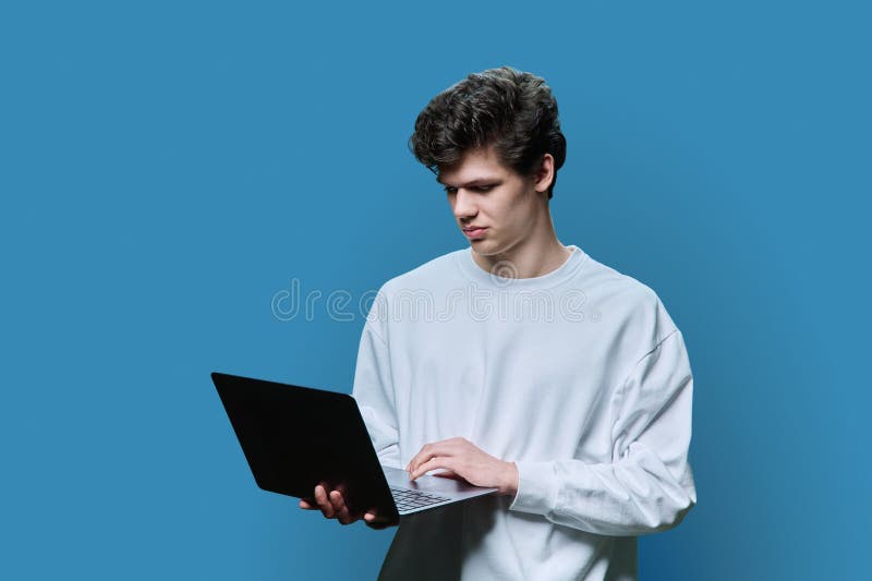 Young male college student using laptop, blue studio background stock photos