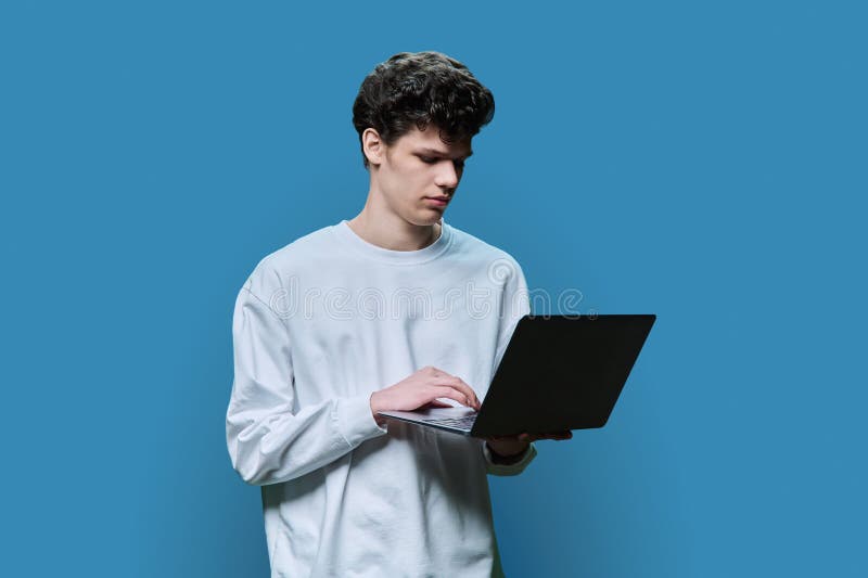 Young male college student using laptop, blue studio background stock photo