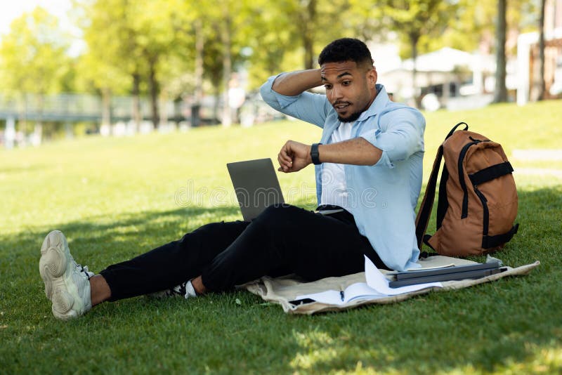 Young male freelance programmer feeling shocked from overtime for doing job via laptop computer, sitting in park stock image