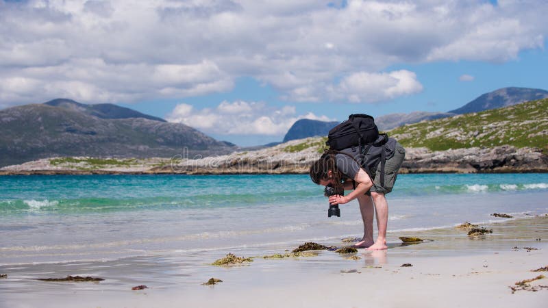 Young male photographer with dreadlocks at a sunny white sand beach