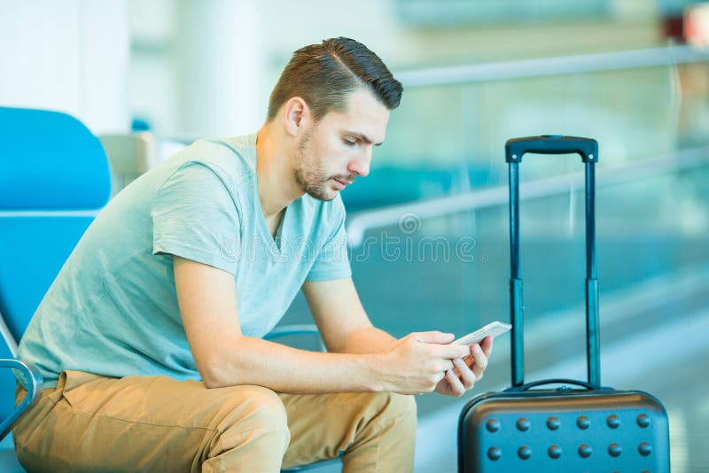 Young man in an airport lounge waiting for flight aircraft. Caucasian man with smartphone in the waiting room