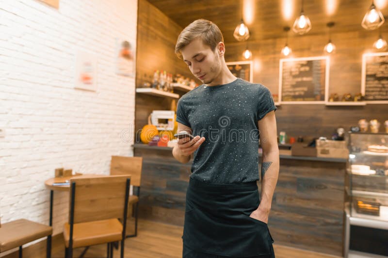 Young man in apron coffee shop worker at bar counter, taking order on smartphone royalty free stock photos Young man in apron coffee shop worker at bar counter, taking order on smartphone royalty free stock photos