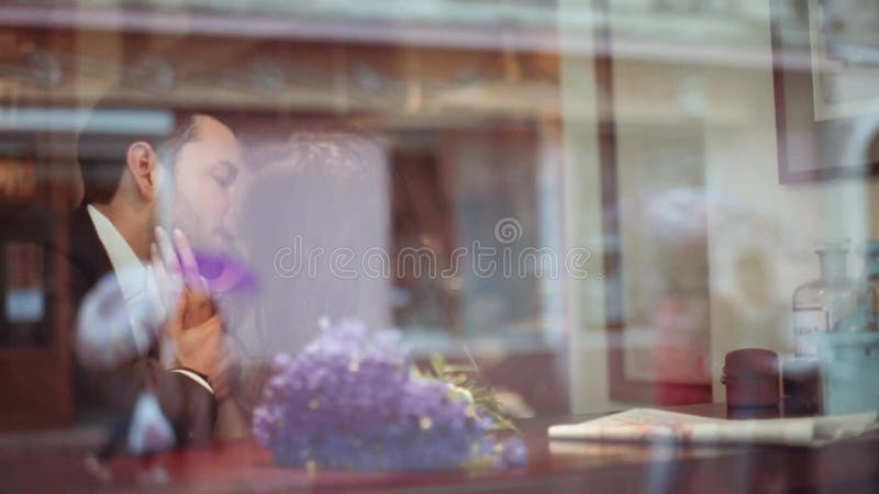 Young man and attractive brunette European woman in the white dress passionately kissing in the cafe by the window in a