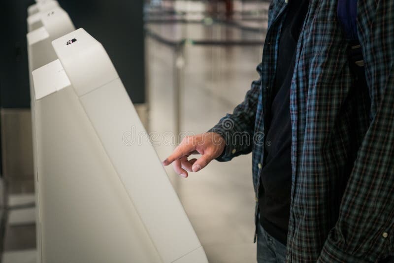 Young man with backpack touching interactive display using self service machine, doing self-check-in for flight or royalty free stock image