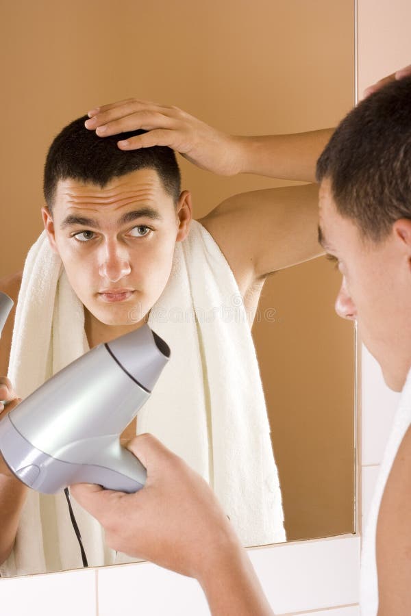 Young man in the bathroom s mirror using hair drier