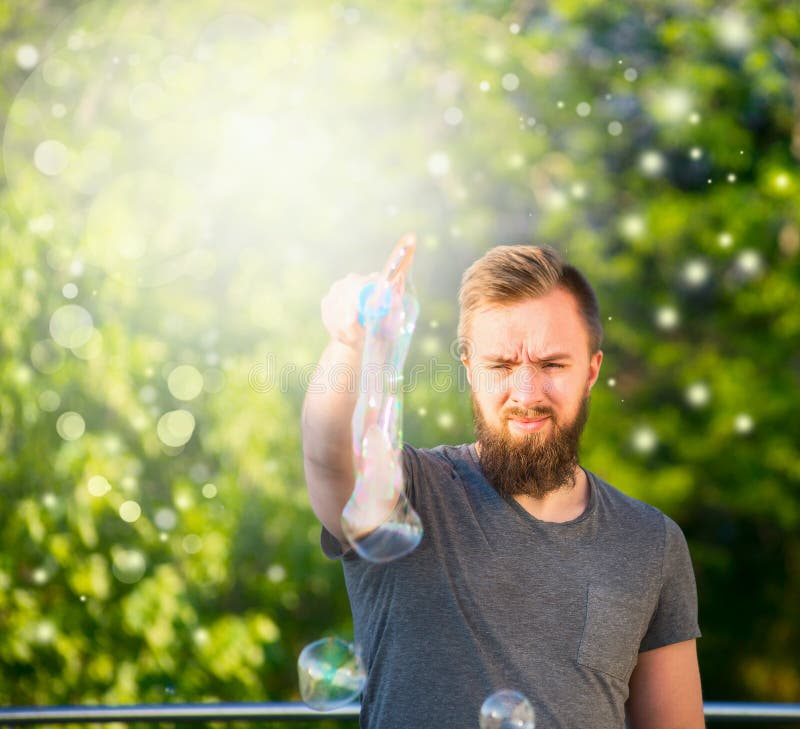 Young man with a beard spending time in nature, making soap bubbles nature background with bokeh stock image Young man with a beard spending time in nature, making soap bubbles nature background with bokeh stock image