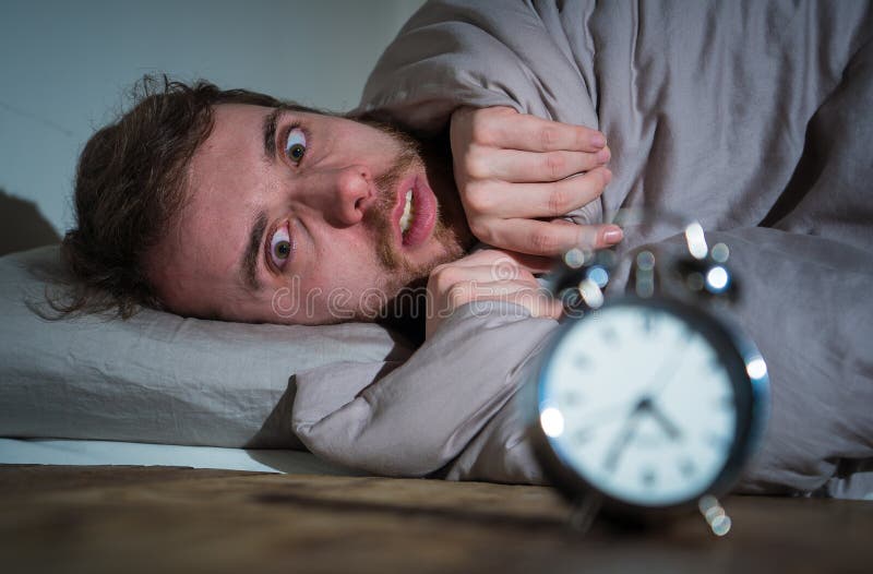 Young man in bed with alarm clock feeling desperate and distress not able to sleep with insomnia royalty free stock image Young man in bed with alarm clock feeling desperate and distress not able to sleep with insomnia royalty free stock image
