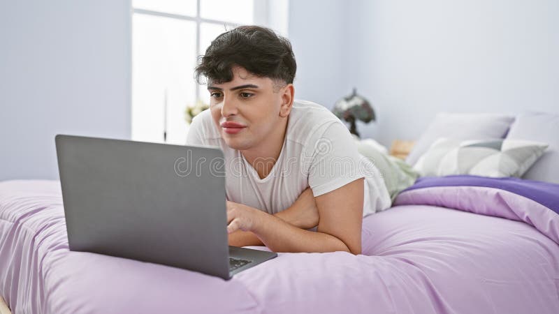 A young man in a bedroom working on a laptop with a thoughtful expression, depicting a casual home setting stock images