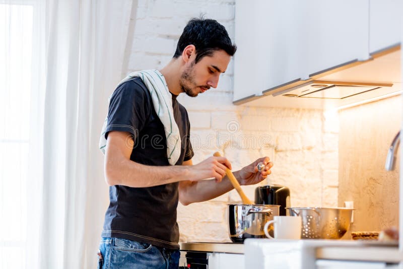 Young man in black shirt cooking at kitchen in home.