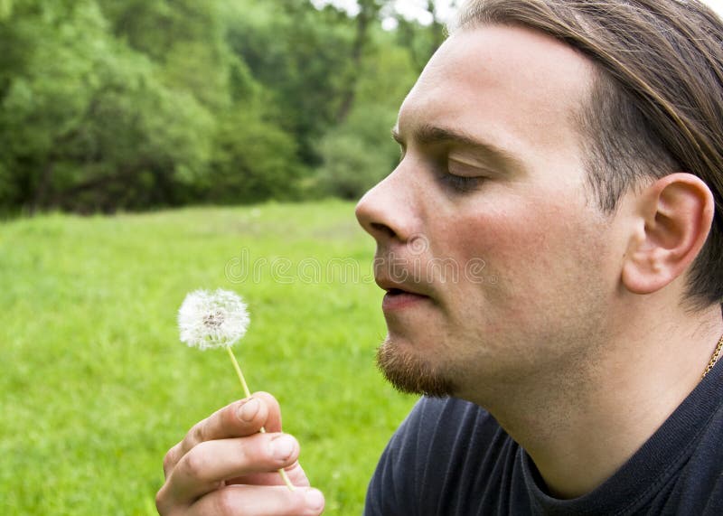 Young man blowing dandelion