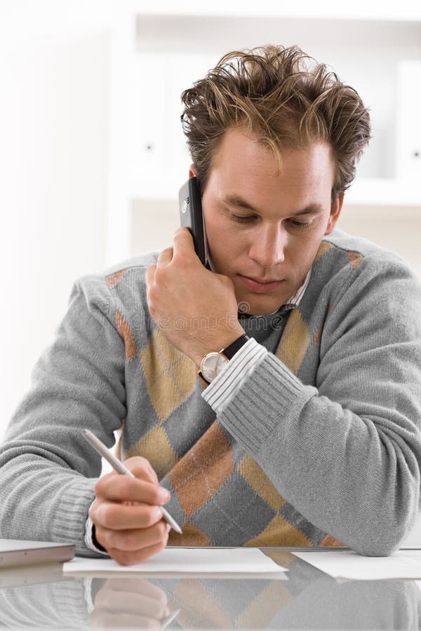 Young man writing and calling on phone at home. Young man writing and calling on phone at home.