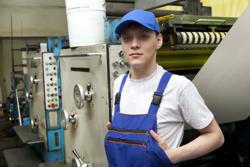 Young man in cap working on offset printing machine stock images