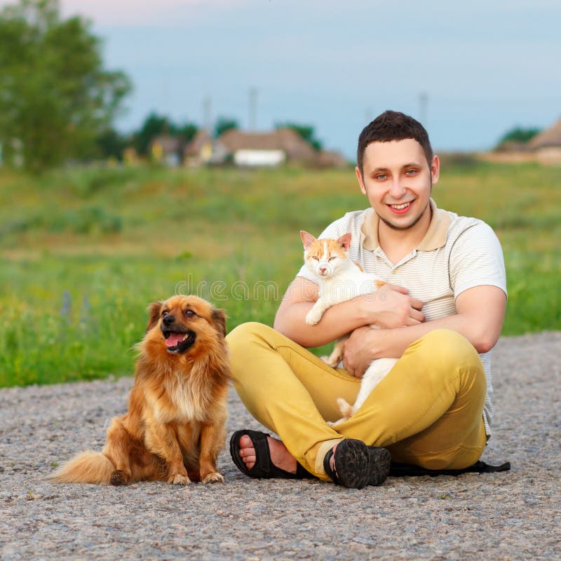 A young man with a cat and a dog are sitting on the road, the gu stock image A young man with a cat and a dog are sitting on the road, the gu stock image