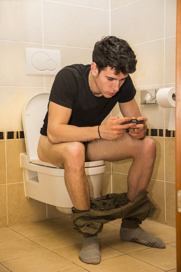 Young Man with Cell Phone Sitting on Toilet.
