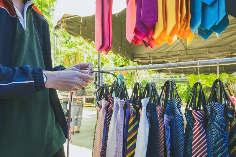 Young man choosing which tie to buy at local market. Many various pattern colorful neckties hanging on clothes rack.  Colorful tie collection in the shop. Fashion accessory. Selective focus on hands