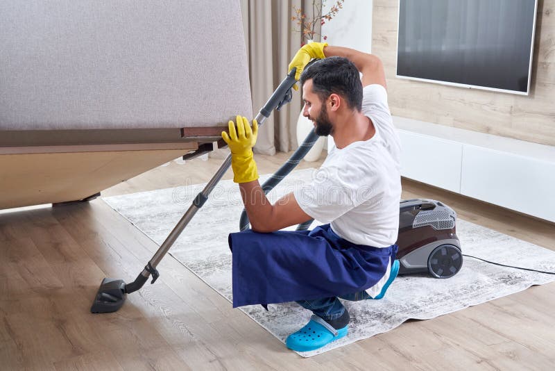 Young Man Cleaning Sofa with Vacuum Cleaner in Leaving Room at Home