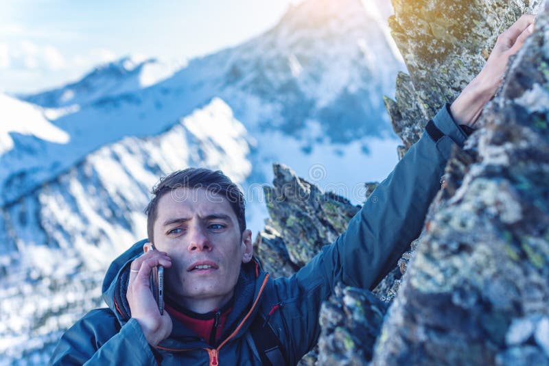 A young man climbs the mountain to the top and talking holding the phone. Concept of persistence and goal achievement royalty free stock image A young man climbs the mountain to the top and talking holding the phone. Concept of persistence and goal achievement royalty free stock image