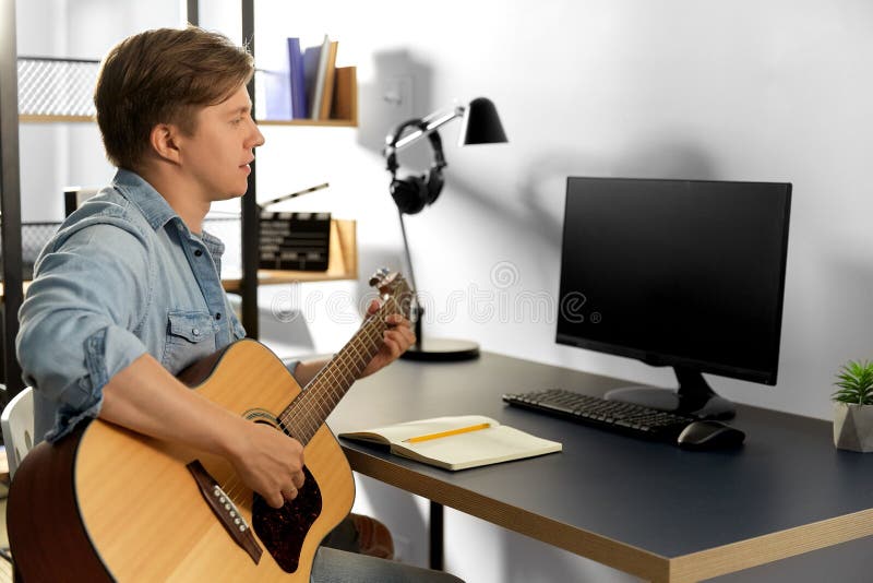 Young man with computer playing guitar at home