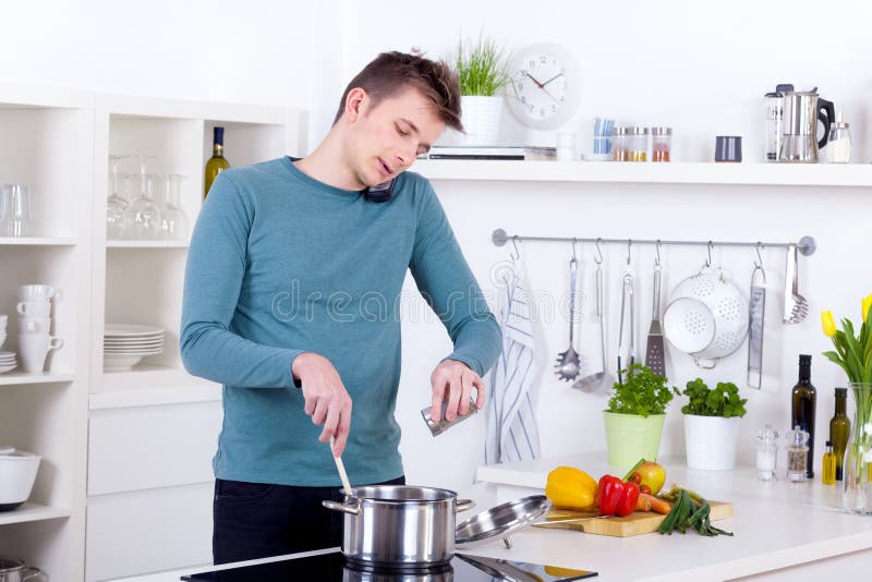 Young man cooking a meal and talking on the phone in his kitchen