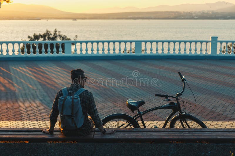 Young Man Cyclist Sitting On The Next To Bicycle Enjoying At The Sunset Vacation Traveling Relaxation Resting Concept royalty free stock photography Young Man Cyclist Sitting On The Next To Bicycle Enjoying At The Sunset Vacation Traveling Relaxation Resting Concept royalty free stock photography