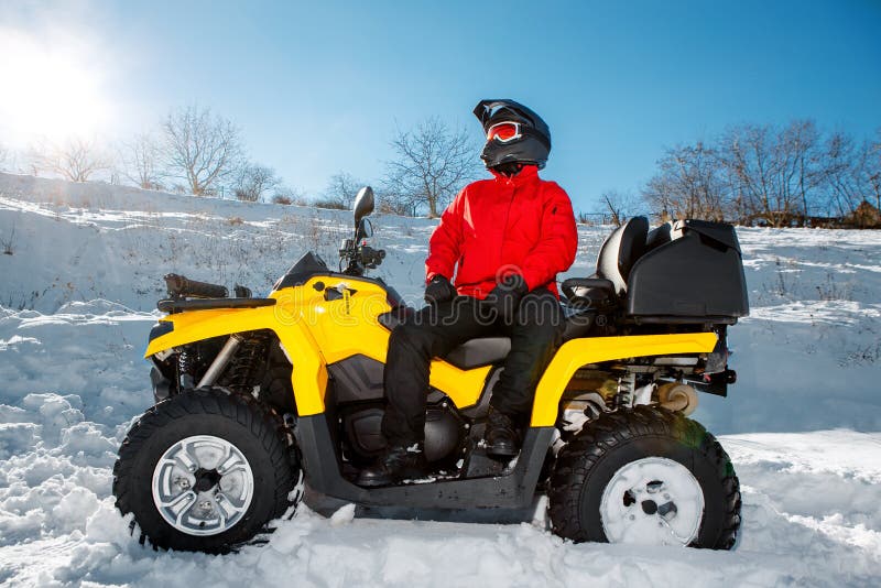 Young man driver in red warm winter clothes and black helmet on the ATV 4wd quad bike stand in heavy snow with deep