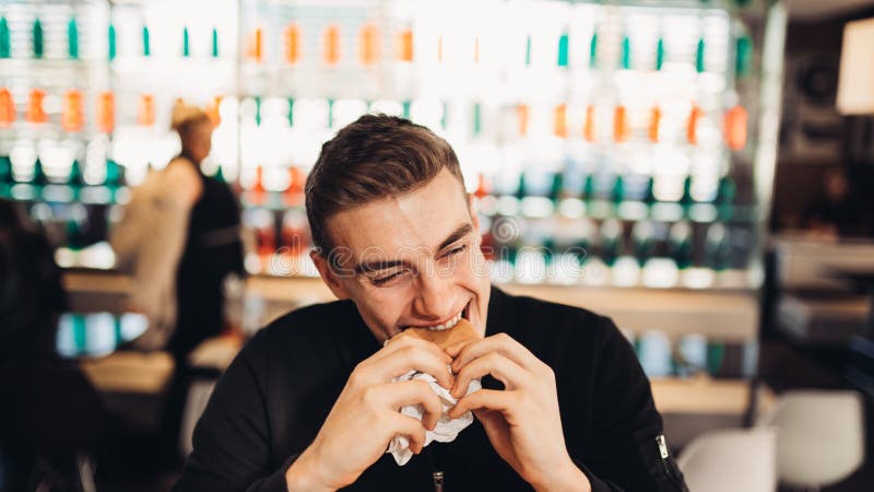 Young man eating fatty hamburger.Craving fast food.Enjoying guilty pleasure,eating junk food.Satisfied expression.Breaking diet