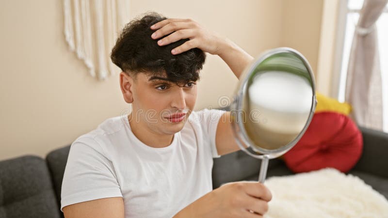 A young man examines his hairstyle in a mirror in the cozy living room of a modern apartment stock images
