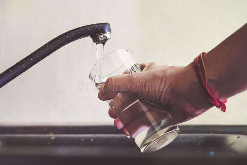 Young man filling up a glass with water in the sink in kitchen at home, a man pours tap water into a glass transparent glass to