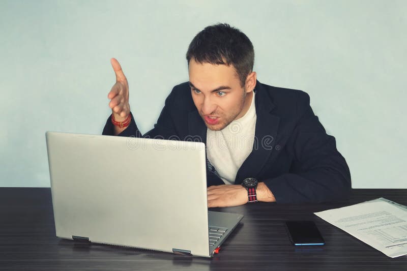 The young man freelancer programmer PC user with a disgruntled bitter angry expression on his face looking at the laptop in front