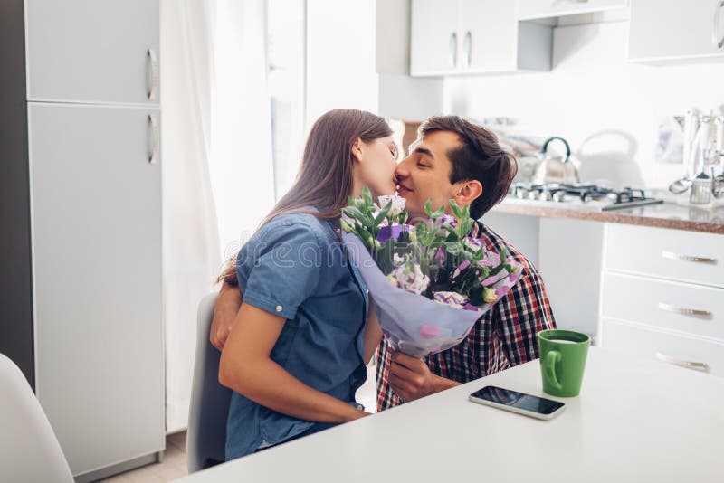 Young man gifting bouquet of flowers to his girlfriend in kitchen. Happy couple hugging. Romantic surprise stock photos Young man gifting bouquet of flowers to his girlfriend in kitchen. Happy couple hugging. Romantic surprise stock photos