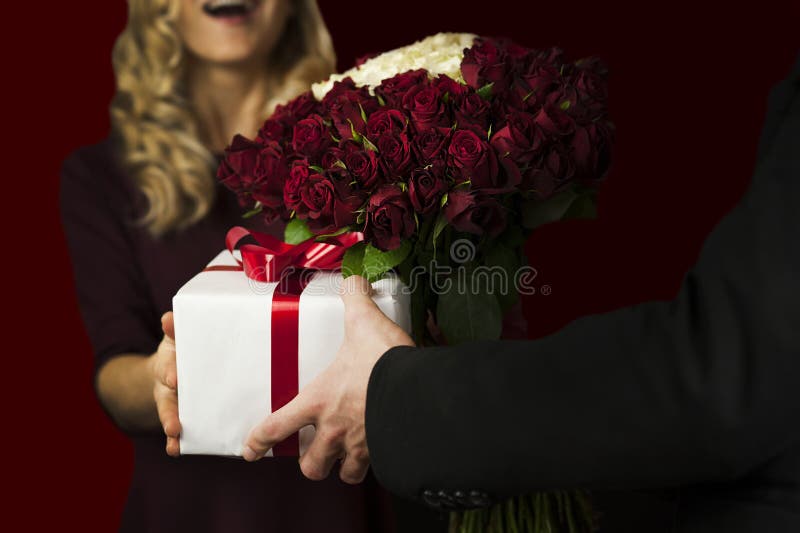 A young man gives a gift a white box with a red bow and flowers to a girl on an isolated black background. Valentine day concept royalty free stock photos A young man gives a gift a white box with a red bow and flowers to a girl on an isolated black background. Valentine day concept royalty free stock photos