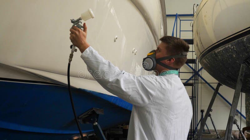 A young man guy is a specialist in cleaning the yacht, in a respirator and using a spray on the background of the yachts. Concep