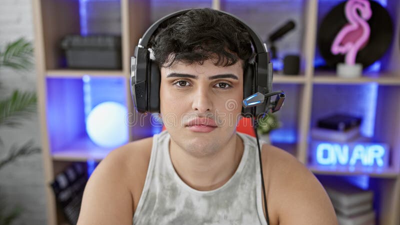 Young man with headphones in a gaming room with neon lights and an \'on air\' sign, looking focused and serious royalty free stock photos