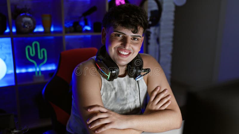 A young man with headphones smiles in a neon-lit gaming room at night, radiating confidence and leisure stock photo