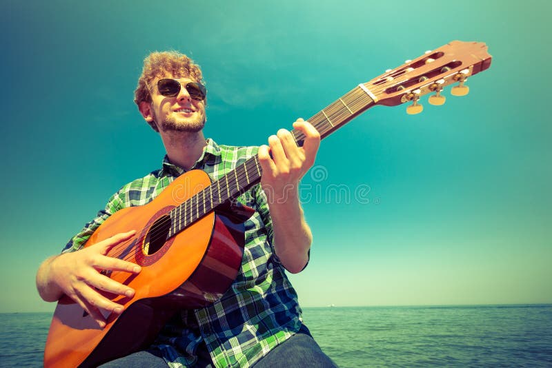 Young man hipster playing guitar by sea ocean.