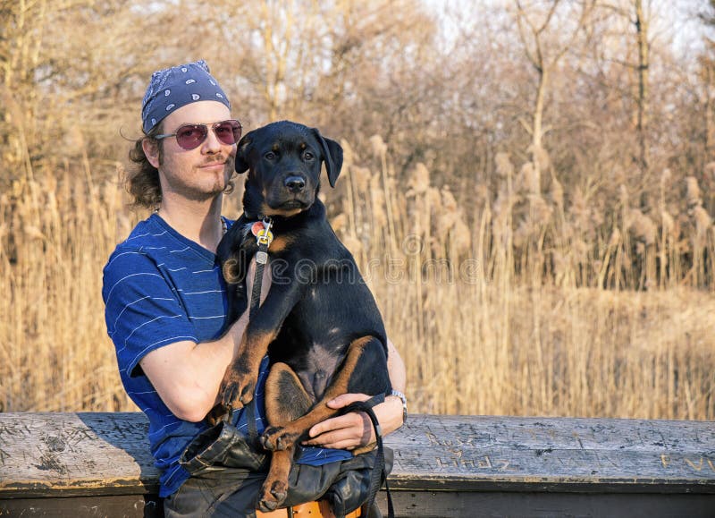 young-man-holding-rottweiler-puppy-portrait-outdoors-77676687.jpg