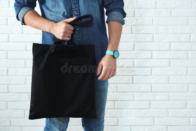 Young man holding textile bag against brick wall, closeup stock images