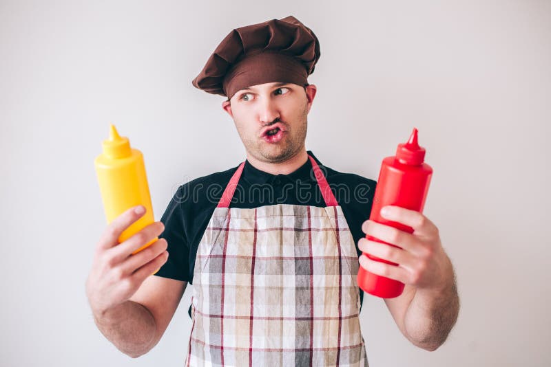 Young man isolated over background. Guy hold colorful bottles with mustart and ketchup in hands. Look on them with funny