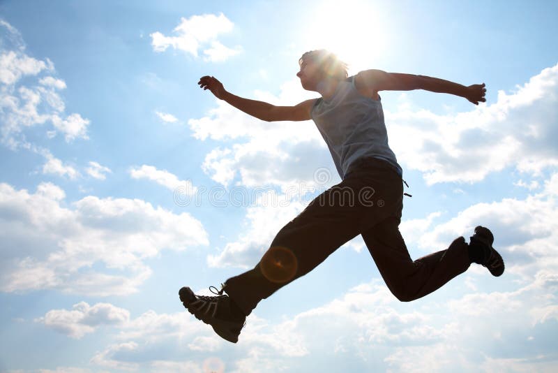 Young man jumping against cloudy sky stock photo