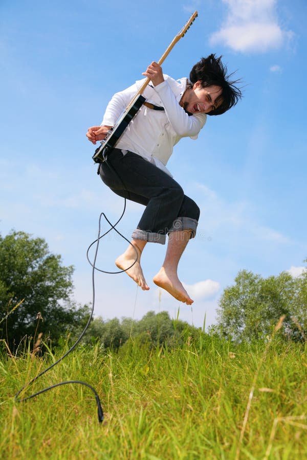 Young man jumps with guitar on grass