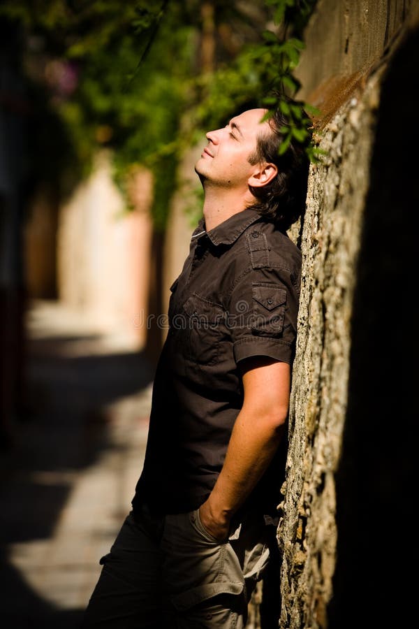 Young man leans stone wall in the street