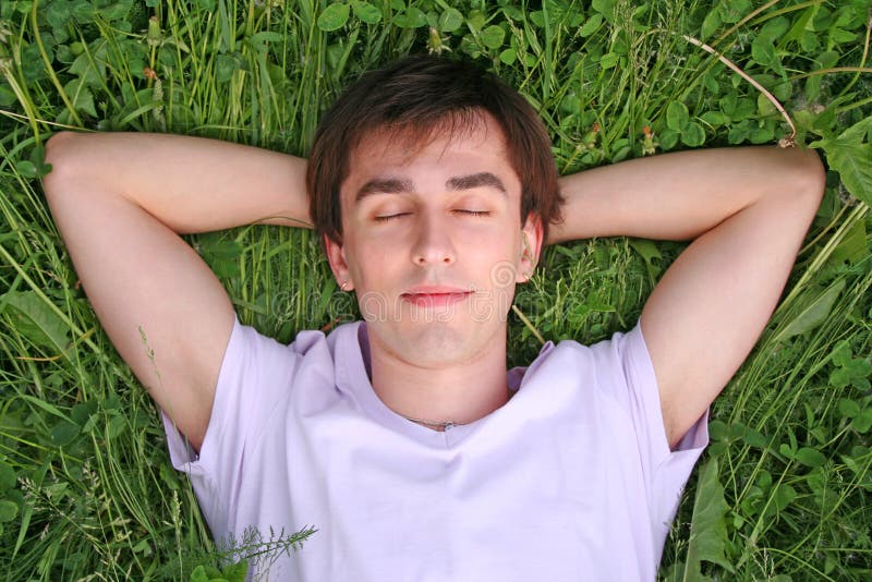 Young man lies on grass head on hands closed eyes