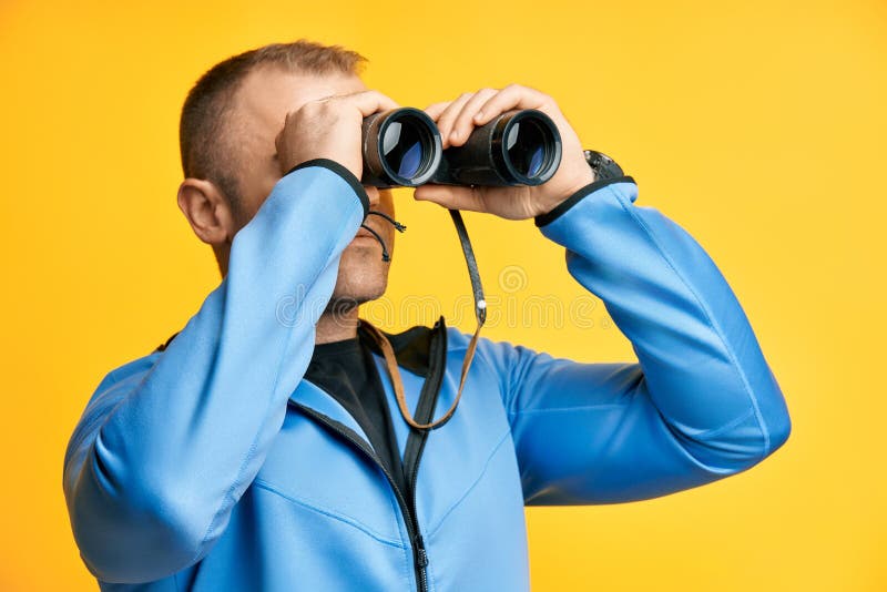 Young man looking through binoculars isolated over yellow background stock images