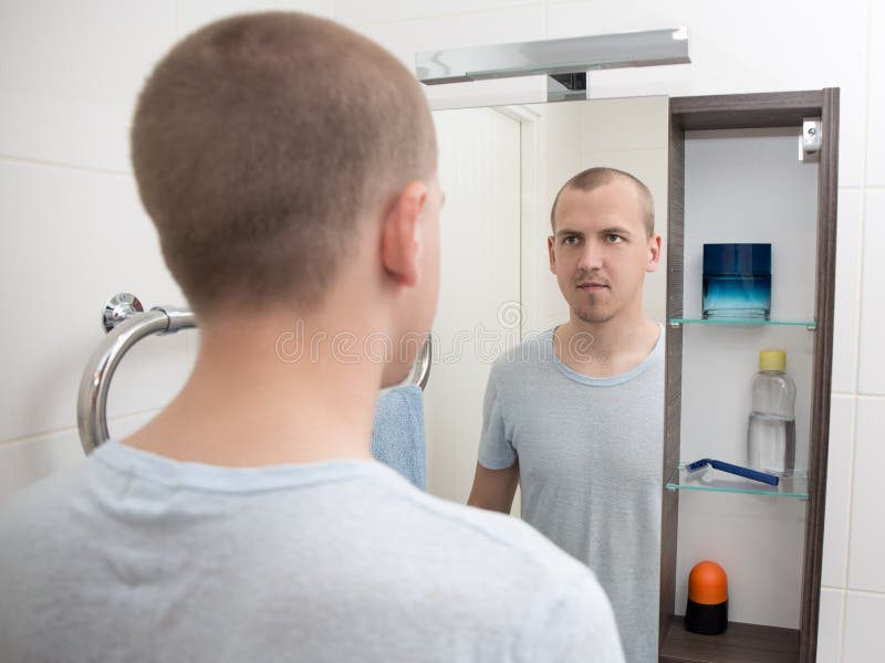Young Man Looking At Mirror In Bathroom Stock Photo - Image: 55380700