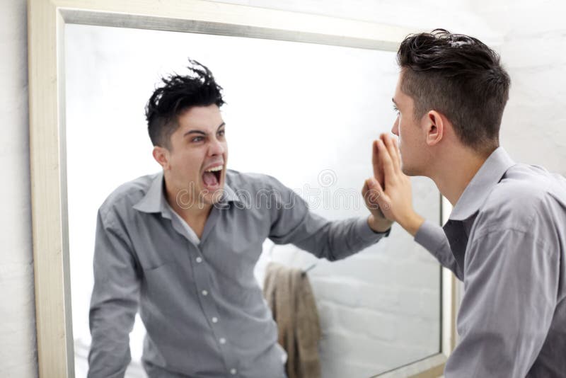 Suppressed emotions. Young man looking at a screaming reflection of himself in a mirror. Young man looking at a screaming reflection of himself in a mirror